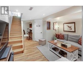 A living room with a staircase on the left and a grey couch with red pillows on the right.
