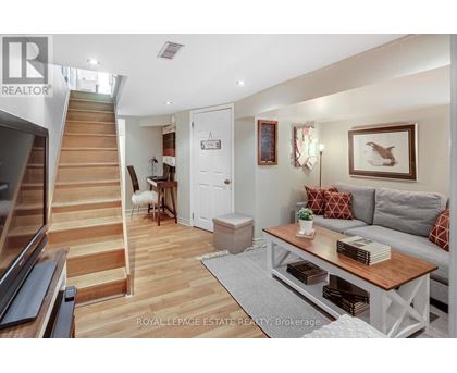 A living room with a staircase on the left and a grey couch with red pillows on the right.