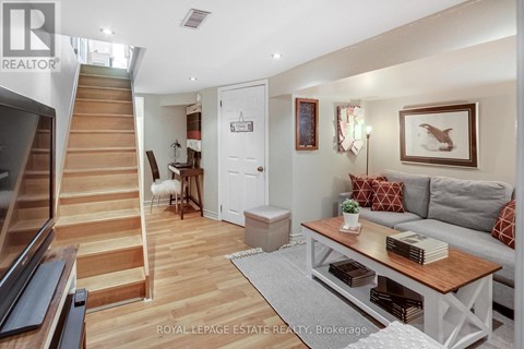 A living room with a staircase on the left and a grey couch with red pillows on the right.