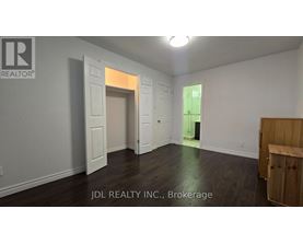 A room with a wooden floor and white walls, with a doorway leading to another room.