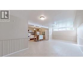 A spacious empty room with a kitchen area in the background.