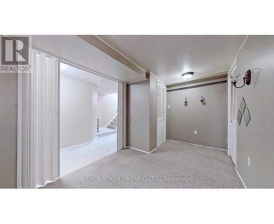 A spacious room with a carpeted floor and a staircase in the background.