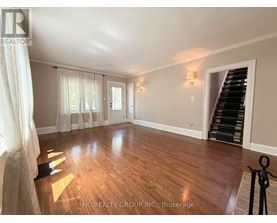 A spacious room with wooden flooring and a staircase on the right side.