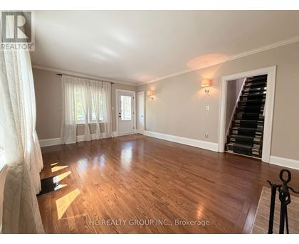 A spacious room with wooden flooring and a staircase on the right side.