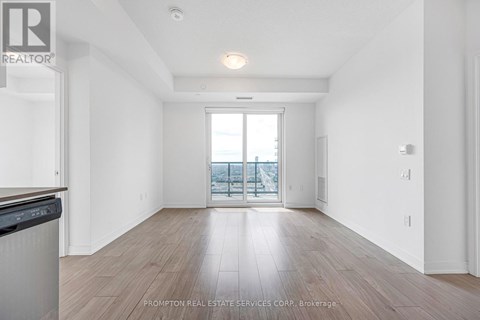 A spacious room with wooden flooring and a large window overlooking a balcony.