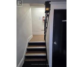 A hallway with a black door on the right and a staircase with wooden steps.