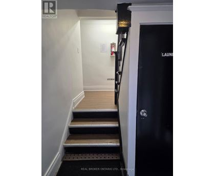 A hallway with a black door on the right and a staircase with wooden steps.