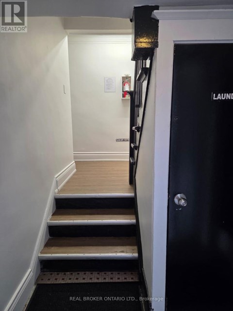 A hallway with a black door on the right and a staircase with wooden steps.