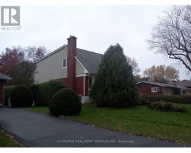 A house with a red brick chimney is surrounded by green bushes and trees.
