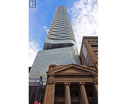A tall glass building stands next to a building with columns.