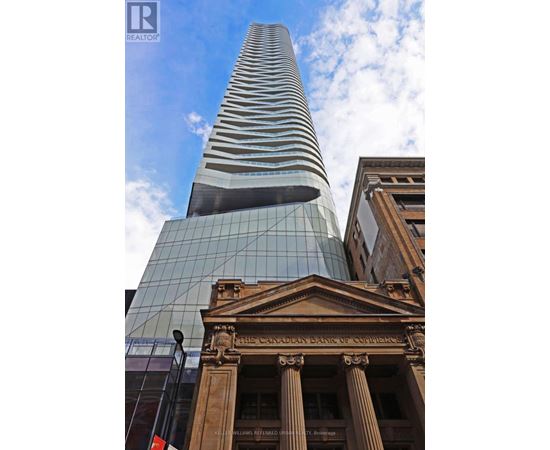 A tall glass building stands next to a building with columns.
