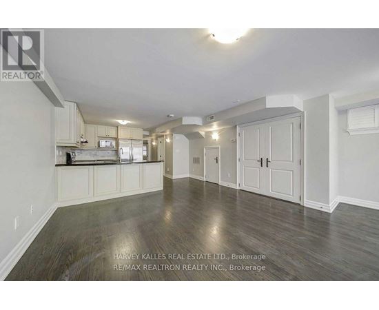 A spacious room with wooden flooring and white walls, featuring a kitchen area with white cabinets and appliances.