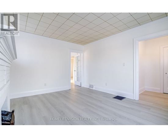 A spacious room with a white ceiling and light wood flooring.