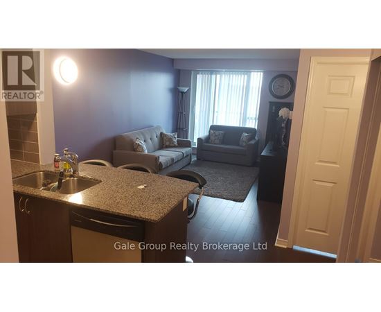 A living room with a grey couch and a kitchen area with a sink and a dishwasher.
