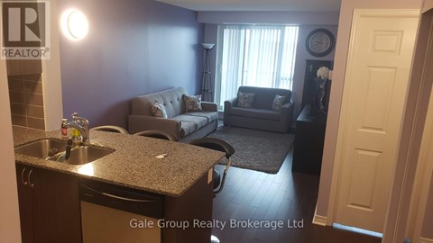 A living room with a grey couch and a kitchen area with a sink and a dishwasher.