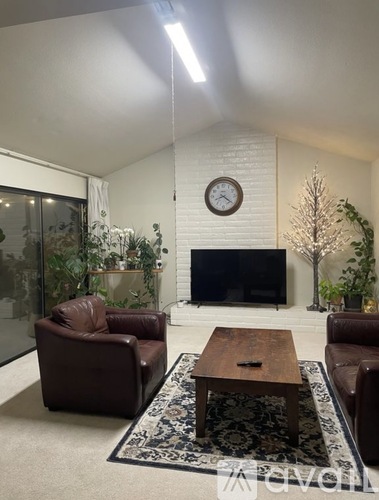 A living room with a brown leather chair, a wooden coffee table, and a flat screen TV mounted on a white brick wall.