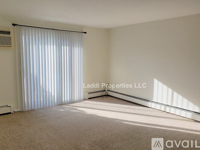 A room with a carpeted floor, a window with blinds, and a wall-mounted air conditioner unit.