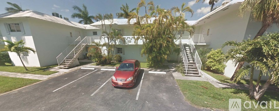 A red car is parked in a parking lot in front of a white building.