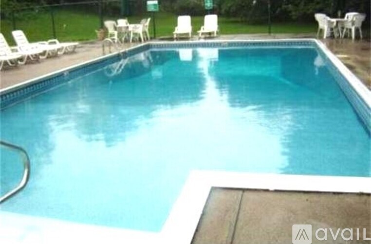 A pool with a blue tinted water and white chairs around it.