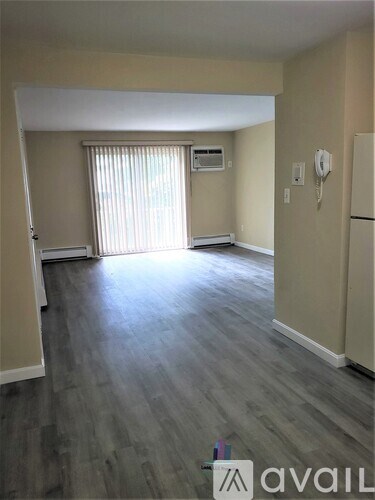 A spacious room with wooden flooring and a window with blinds.