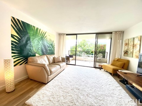 A living room with a large couch and a painting of a palm leaf on the wall.