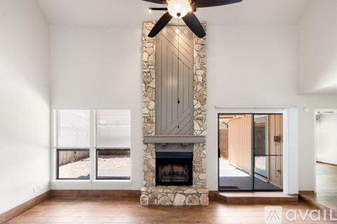 A modern living room with a stone fireplace and a ceiling fan.