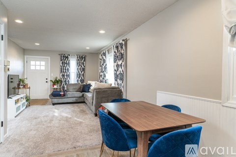 A living room with a grey couch and a wooden dining table with blue chairs.