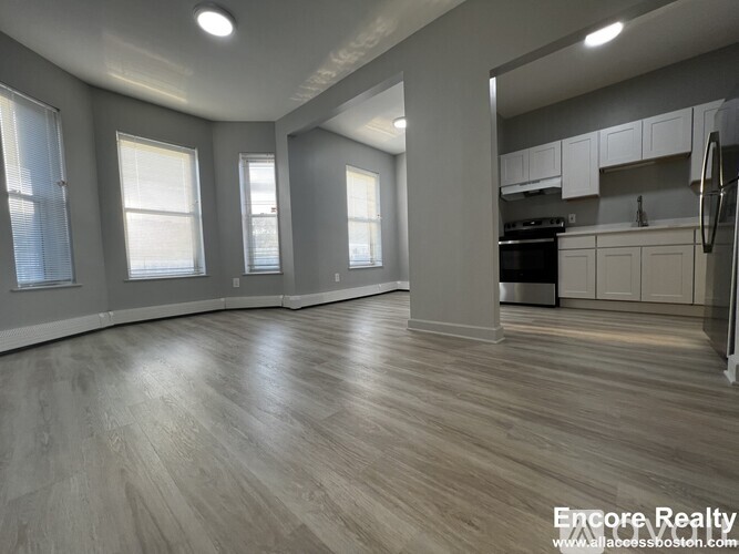 A spacious kitchen and living room with wood flooring and white walls.