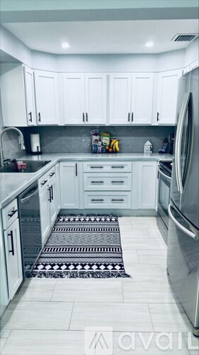 A kitchen with white cabinets and a black and white patterned mat on the floor.