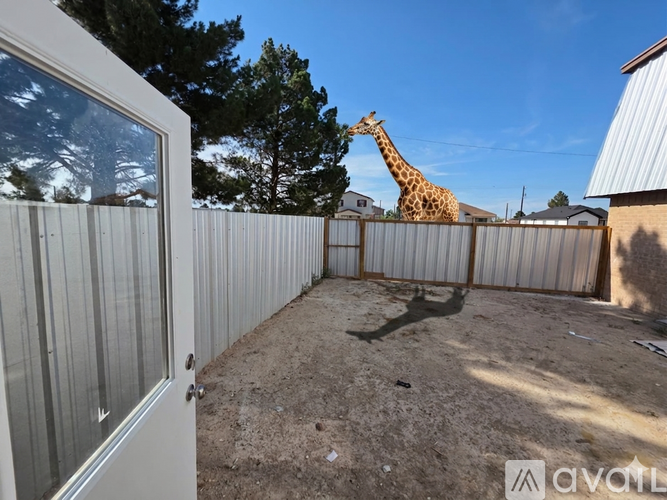 A giraffe is standing in a fenced area with a building in the background.