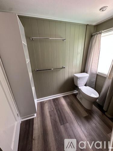 A bathroom with a toilet, a shower with a glass door, and a window with a curtain.