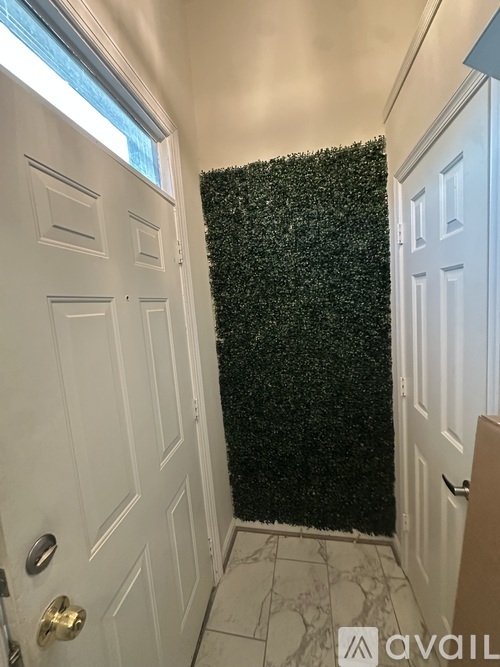 A hallway with a white door and a green hedge wall.