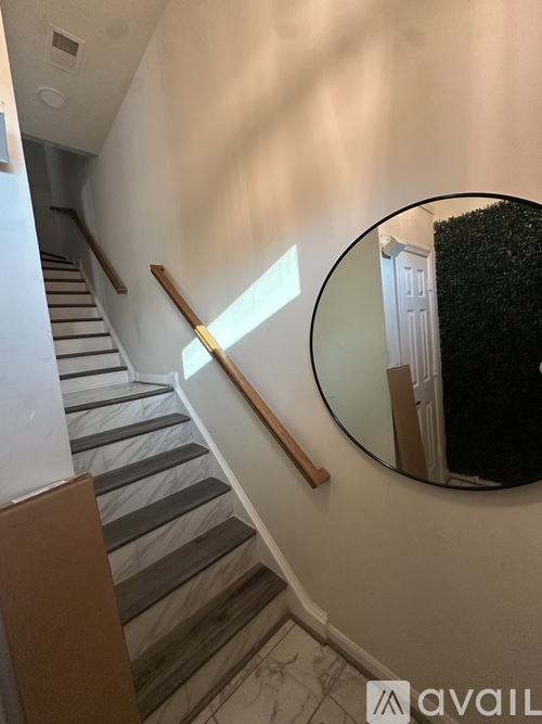 A staircase with a wooden handrail and a round mirror on the wall.
