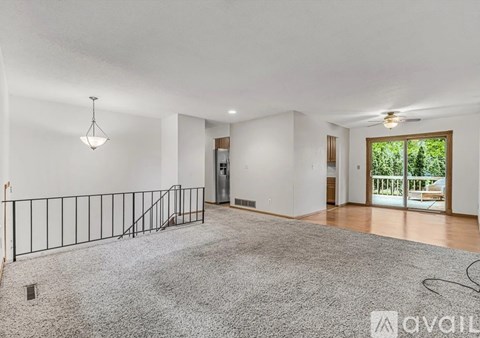 A spacious living room with a grey carpet and a staircase with a metal railing.