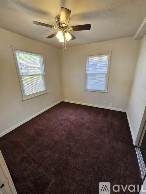 A room with a ceiling fan and two windows.