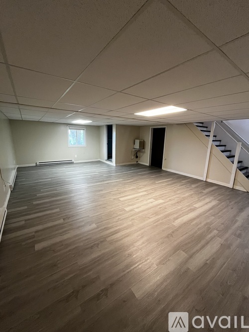 A spacious room with wooden flooring and a staircase.