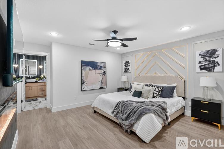 A bedroom with a large bed, a ceiling fan, and a painting on the wall.