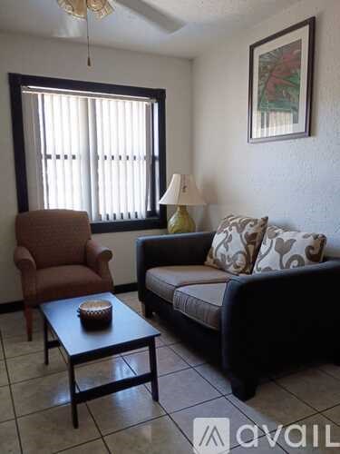 A living room with a brown chair, a black couch, and a table with a bowl on it.