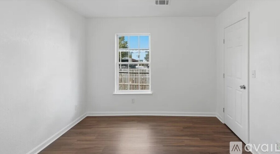 A room with a window showing a view of trees and a white door on the right.
