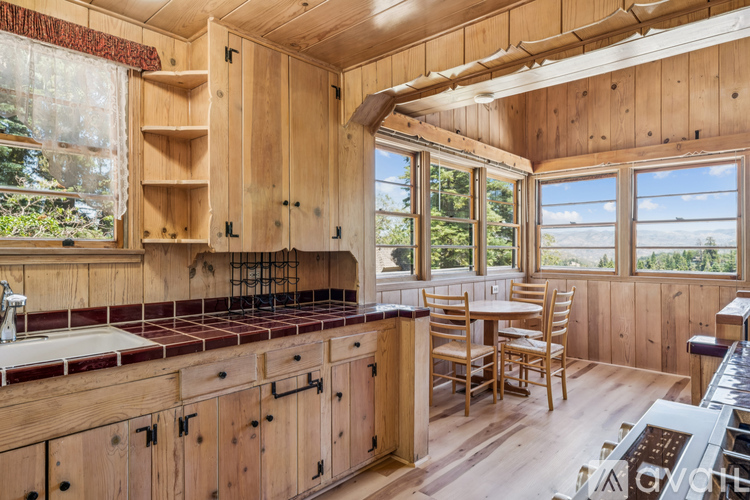 A kitchen with wooden cabinets and a window overlooking a forest.