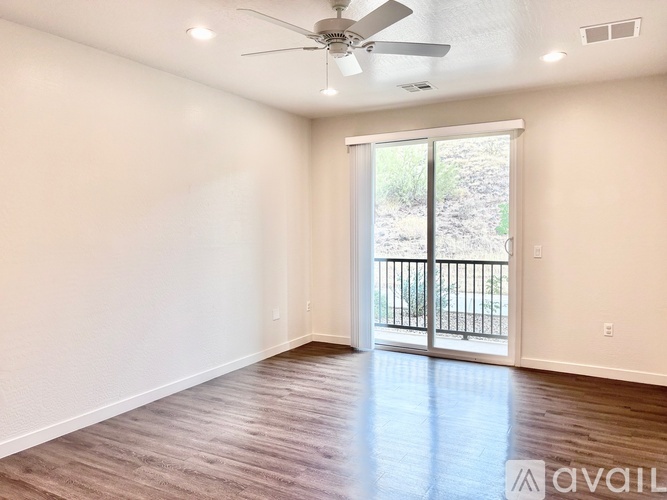 A spacious room with a ceiling fan and sliding glass doors leading to a balcony.