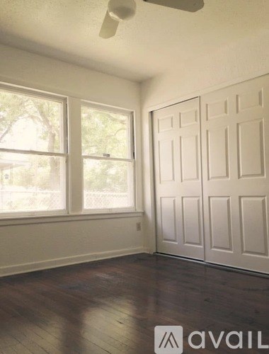 A room with a white door and a window with a view of trees outside.