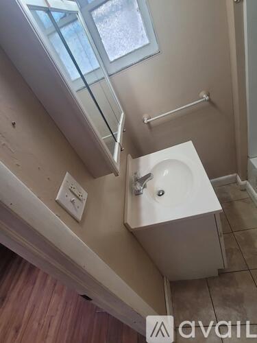 A small white sink in a bathroom with a window above it.
