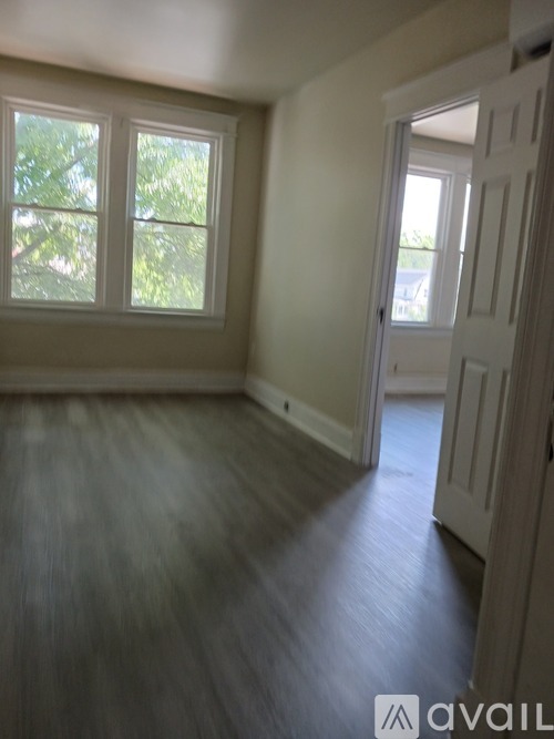 A room with a white door and a window with a view of trees.