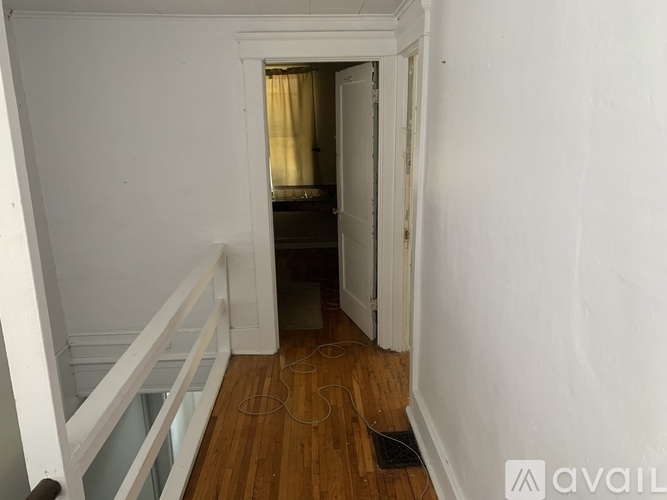 A hallway with a wooden floor and white walls leading to a bedroom.