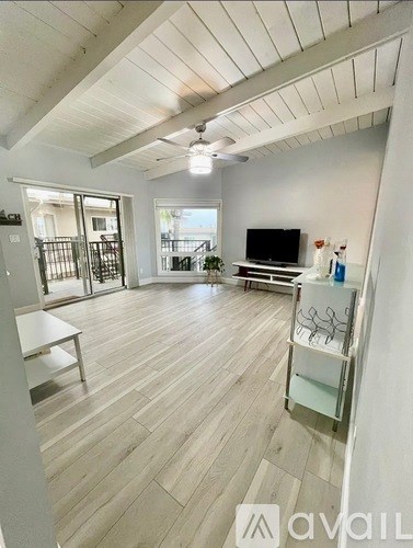 A spacious living room with a television and a sliding glass door leading to a balcony.