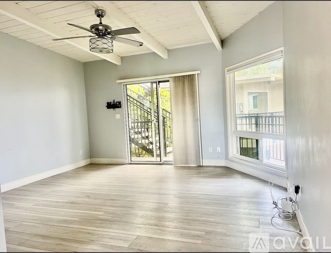A spacious room with a ceiling fan and sliding glass doors leading to a balcony.