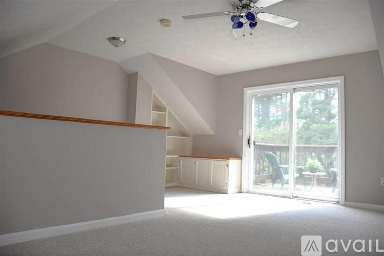 A room with a ceiling fan and a window with a view of trees.