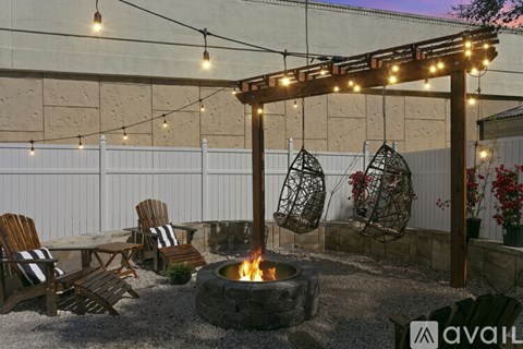 A patio with a fire pit and chairs under a string of lights.
