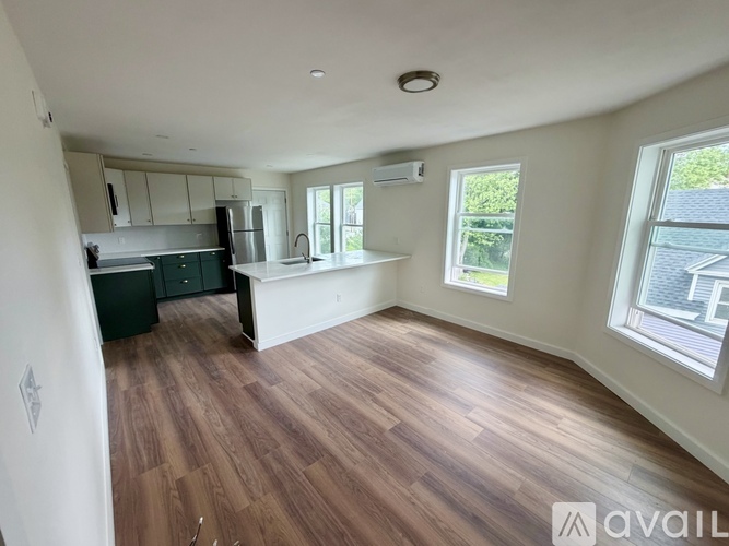 A spacious room with wooden flooring and a kitchen area with white appliances.
